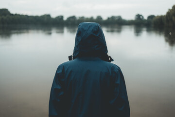 Person in einer Regenjacke schaut auf einen See bei trübem Regenwetter