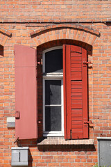 Fototapeta na wymiar Alter roter Fensterladen und Fenster aus Holz an einer roten Backsteinmauer, Lübeck, Deutschland, Europa