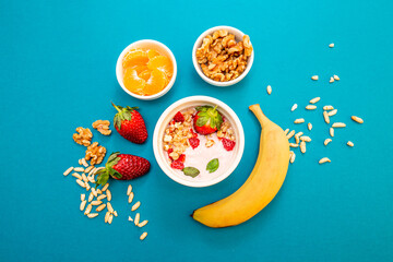 Healthy breakfast with granola and fruits, in white bowls, with a light blue background. 