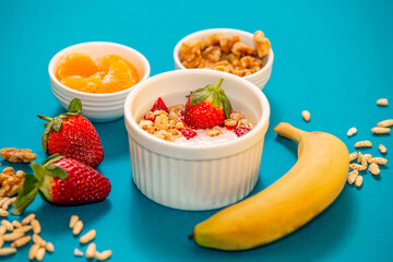 Healthy breakfast with granola and fruits, in white bowls, with a light blue background. 