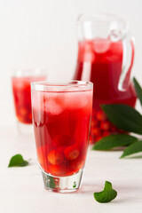 Summer delicious refreshing compote of cherries with pulp and with ice in glasses on a white background, a jug with a drink