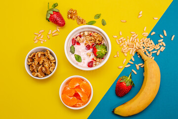 Healthy breakfast with granola and fruits, in white bowls, with a yellow and light blue background. 