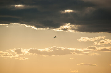 Unique beautiful dramatic gray and white clouds on light blue sky on daylight. The silhouette of airplane rising upward the clouds after takeoff. Air travel concept.