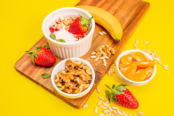 Healthy fit breakfast with granola and fruits on a wooden table, in white bowls, with a yellow background. 