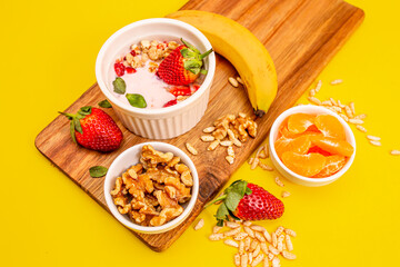 Healthy fit breakfast with granola and fruits on a wooden table, in white bowls, with a yellow background. 