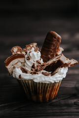 homemade cupcake with white cream and chocolate with nuts on a dark background
