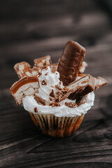 homemade cupcake with white cream and chocolate with nuts on a dark background