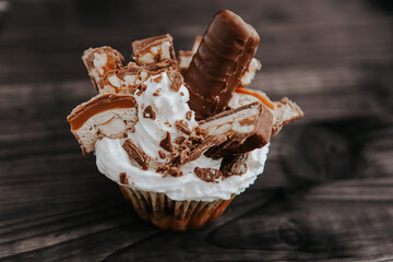 homemade cupcake with white cream and chocolate with nuts on a dark background