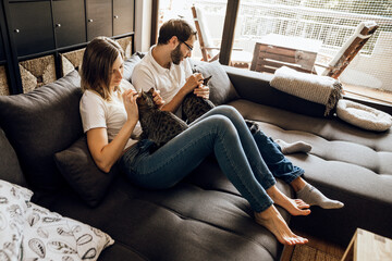 Obraz premium Close up of young couple with adorable cat sitting on sofa