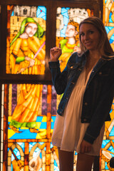 Fototapeta premium Young blonde caucasian woman in a white dress and denim jacket enjoying a beautiful medieval hotel in the town of Olite in Navarra. Spain, rural lifestyle. In a stained glass window