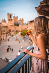 Fototapeta na wymiar Young blonde caucasian woman in a long pink dress enjoying a beautiful rural hotel in Olite in Navarra. Spain, rural lifestyle. With a soft drink on the terrace and a castle in the background