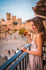 Young blonde caucasian woman in a long pink dress enjoying a beautiful rural hotel in the town of Olite in Navarra. Spain, rural lifestyle. Having a drink with a castle in the background