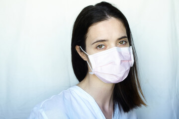 A woman in gloves and a protective mask stands on a light background in a white jacket. The concept of suppression of coronavirus