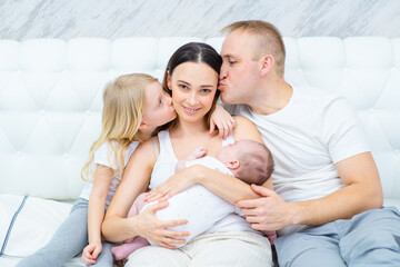 A newborn boy lies in his mother’s arms, a newborn hugs the mother of the newborn and the baby himself, and the older sister sits next to the mother. Happy family concept