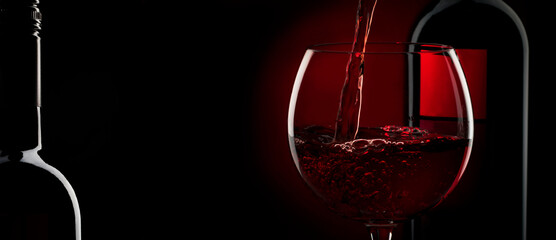 Pouring red wine into the glass against red black background. Panoramic banner with copy space