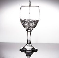 Pour water into half a glass of wine, creating bubbles on a gray background.