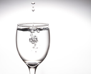 A tall glass, a glass of wine with clear water with bubbles floating in the mouth of the glass Inside on a gray background