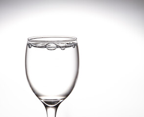 Tall glass, wine glass with clear water There are bubbles floating in the mouth of the glass. Inside on a gray background
