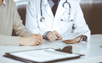 Unknown male doctor and patient woman discussing something while sitting in clinic and using tablet computer. Best medical service in hospital, medicine, pandemic stop