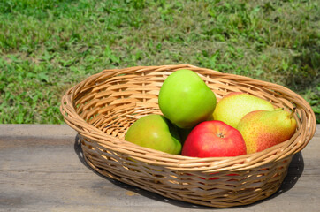 Apples and pears in a wicker basket on a rough wooden table.