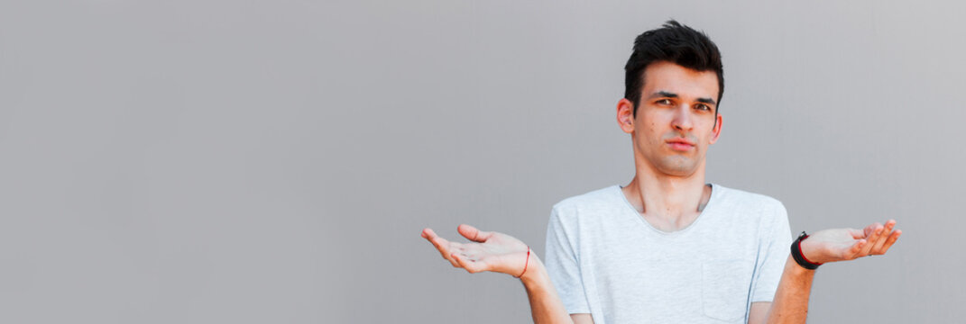 Portrait Of Beautiful Young Man With Trendy Hair Looking In Camera With Confused Emotion, Spreading Hands. Guy Don't Know What To Answer His Girlfriend.