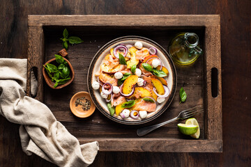 Refreshing summer salad with smoked salmon, peaches, mozzarella, red onion and basil. Wooden background.