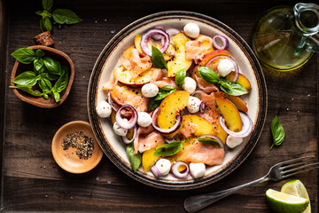Refreshing summer salad with smoked salmon, peaches, mozzarella, red onion and basil. Wooden background.