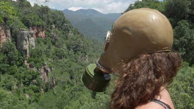 Woman in a gas mask observes a mountainous landscape