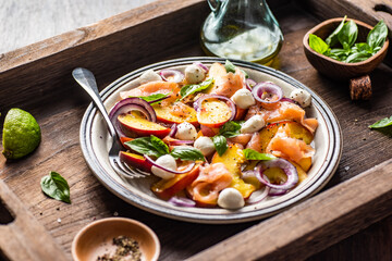 Refreshing summer salad with smoked salmon, peaches, mozzarella, red onion and basil. Wooden background.
