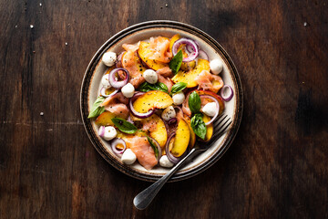Refreshing summer salad with smoked salmon, peaches, mozzarella, red onion and basil. Wooden background.