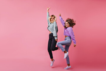 Full-length shot of jumping white girls expressing happy emotions. Studio photo of best friends funny dancing together.
