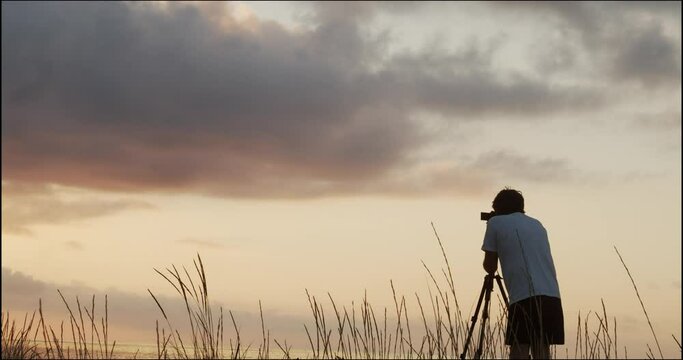 Silhouette of a male photographer with a tripod taking photos during sunrise in nature