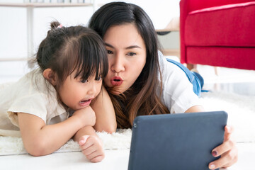 asian beautiful mother lying on the carpet and watching cartoon in tablet with her young daughter. family together and relationship