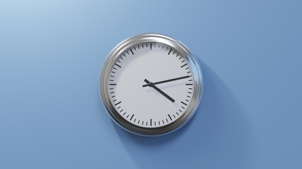 Glossy chrome clock on a blue wall at thirteen past four. Time is 04:13 or 16:13