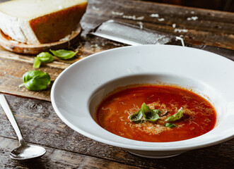 Tomato soup with fresh basil and grated cheese. Rustic table background.