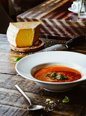 Tomato soup with fresh basil and grated cheese. Rustic table background.