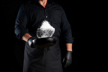 man in a black uniform holding a round cast iron pan with salt
