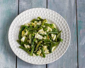 Protein light salad with green beans and chicken eggs on a white plate on a wooden blue table