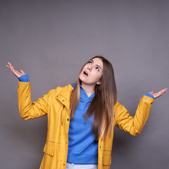 A young white lady in a yellow raincoat raised her hands up, soon it will rain.