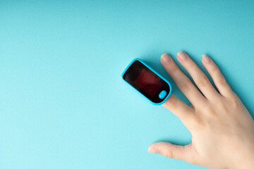 An essential medical device for hypoxia. Female finger in a pulse oximeter on a blue background...