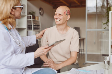 Warm toned portrait of smiling bald woman talking to female doctor during consultation on alopecia...
