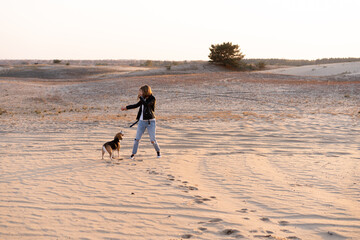 Fototapeta na wymiar a young Caucasian girl somewhere in a leather jacket and blue jeans runs along the sandy beach with her beagle dog