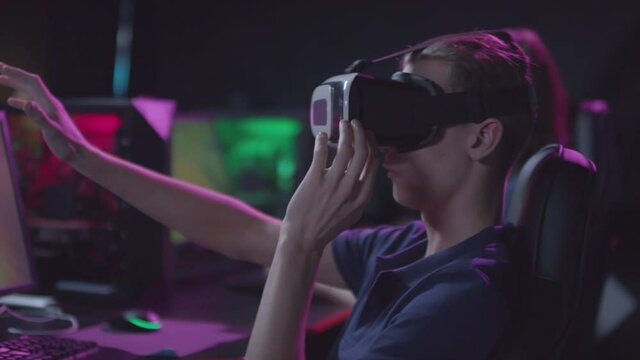 Handheld side view shot footage of young guy wearing VR headset playing video game in cybersport club