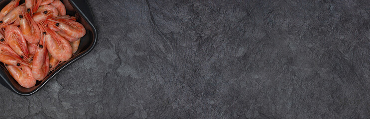 Shrimp salad bowl on a black slate stone stand. Juicy boiled shrimp. Dark background. Long high resolution image