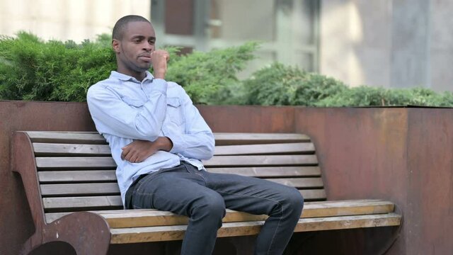 Sick Young African Man Coughing on Bench Outdoor