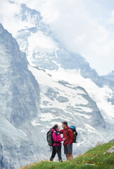 Loving couple with backpacks hugging, beautiful mountains scenery on background. Mountain hiking, tourists reaching peak together. Wild nature with amazing views. Sport tourism in Alps.