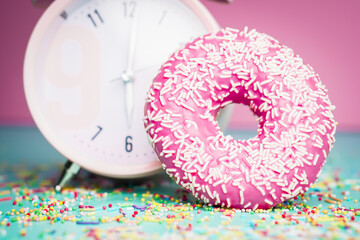 Pink sweet donut with decoration on colourful background.