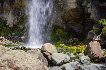 Powerful stream of Taranaki falls splashes into shallow pool amongst rocks