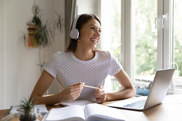 Overjoyed young female student in headphones have fun preparing homework using laptop, happy...