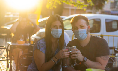 Spain Madrid. Caucasian couple toasting with beer wearing sanitary mask. Reopen pubs and club after quarentine coronavirus Covid-19. Man and woman drinking beer. Cheers. People smiling wearing mask
